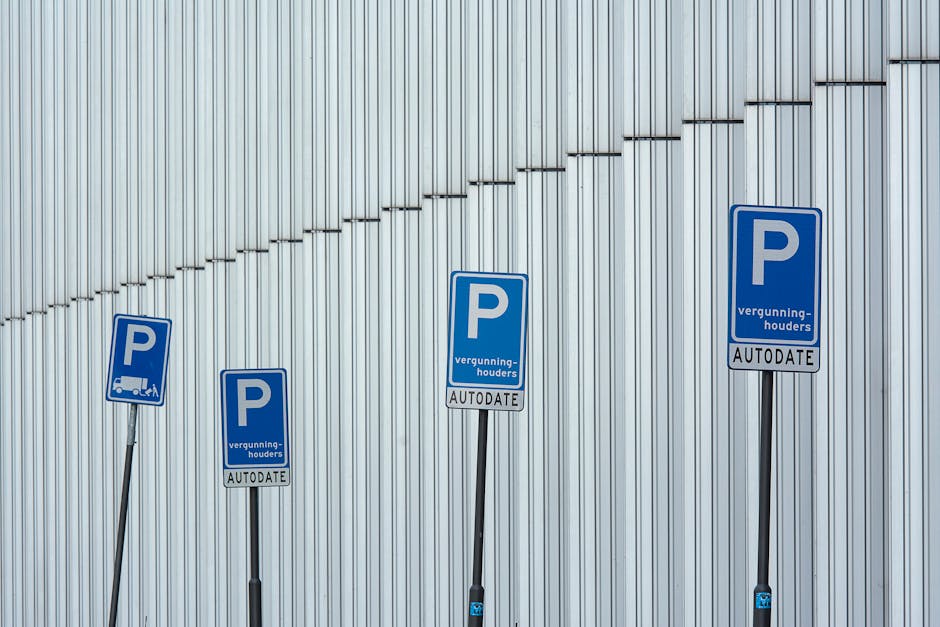 Four blue parking permit signs mounted on black metal poles positioned against a vertically corrugated metal wall. The signs display a large white letter 'P' with additional text including 'vergunninghouder' and 'AUTODATE' underneath. The signs are aligned in a row, with the largest sign in the center and smaller signs to the left and right, indicating designated parking areas for vehicle loading or moving purposes. The environment suggests an urban setting, possibly near a commercial or industrial building, relevant to house removals or moving logistics. As part of the home relocation process, these parking permits support parking management during furniture transport or packing and moving activities, with signage from Man and Van Bounds Green visible in the context of residential relocations within the Bounds Green area, as per the associated webpage.